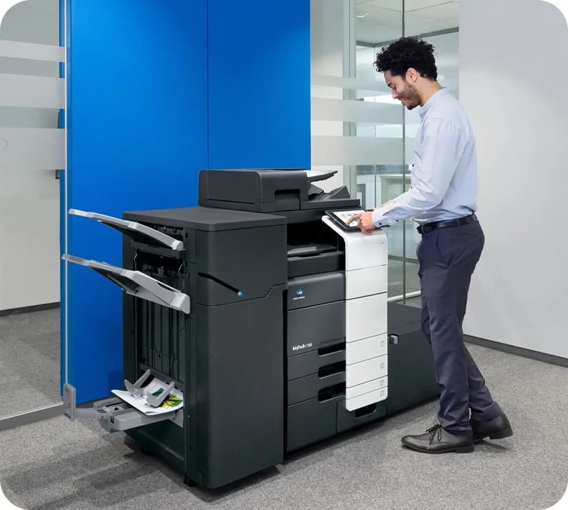 A DNC customer using the touchscreen on a Konica Minolta bizhub multifunction printer in an office
